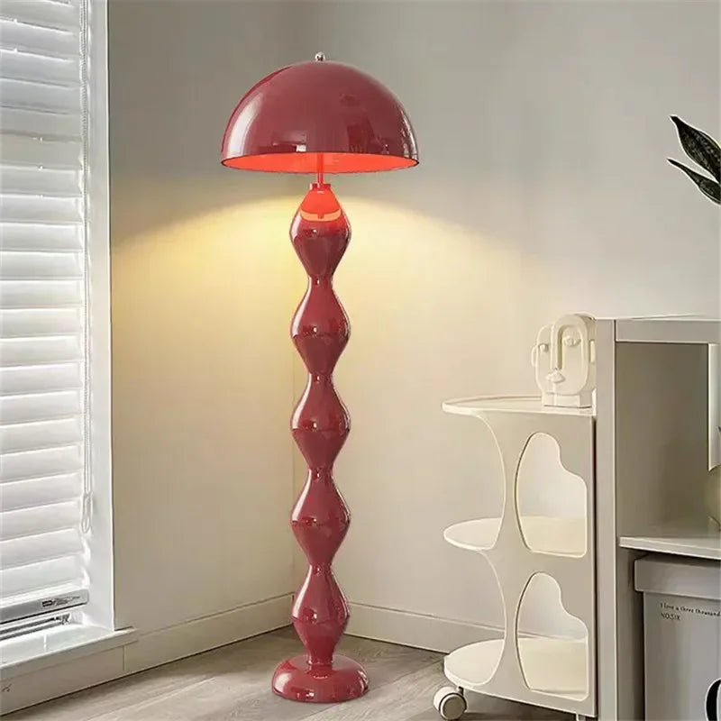 Red floor lamp in a room with a shelf and window blinds.