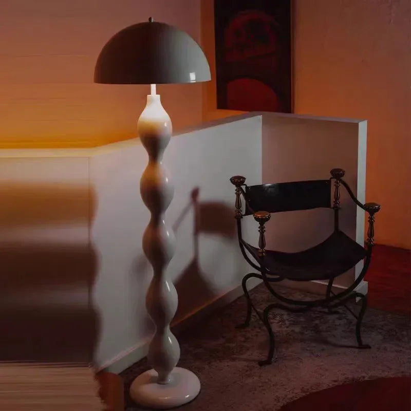 White floor lamp with black shade next to a black chair in a dimly lit room.