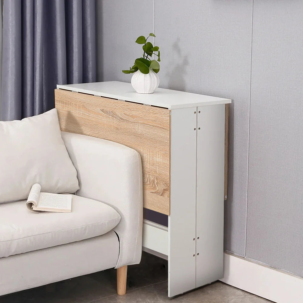 White and wooden foldable dining table with a plant next to a gray sofa against a gray wall.