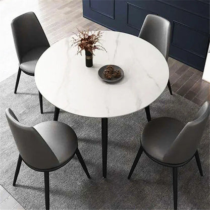 Round marble affect dining table with four gray chairs in a room with dark blue walls.
