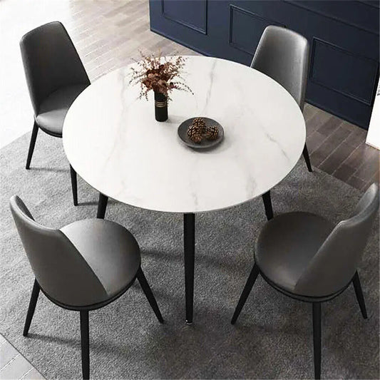 Round marble affect dining table with four gray chairs in a room with dark blue walls.