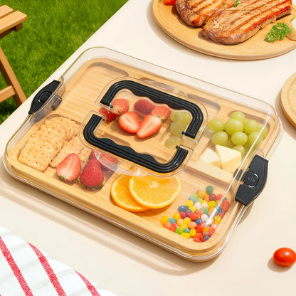 Wooden snack tray with fruits, crackers, and candies on a picnic table.