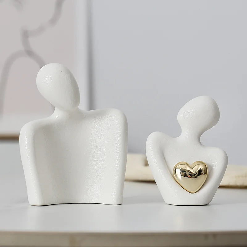Two white ceramic figures with a gold heart on a light background