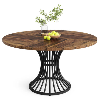 A round dining table with a dark brown wood top and a black metal wire pedestal base, styled with a glass vase of greenery and a bowl of green apples on a white background.