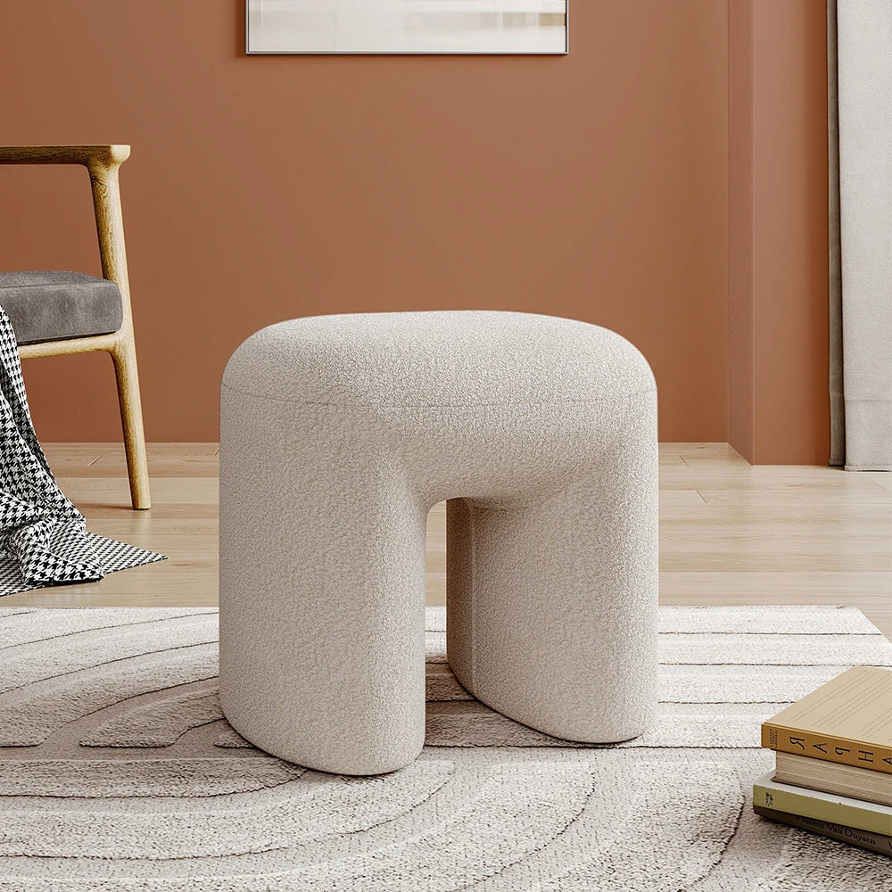Beige / white teddy textured stool in a room with a chair and books on a rug.
