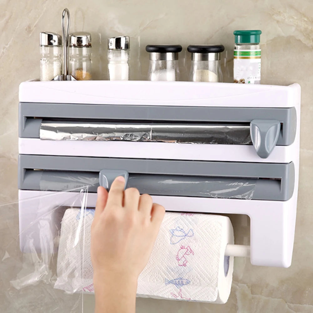 Hand using a kitchen roll holder with a paper towel and plastic wrap dispenser on a tiled wall.