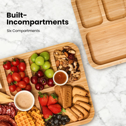 Wooden tray with compartments filled with fruits, nuts, and cookies on a marble surface.
