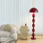 Red floor lamp in a living room setting with a beige armchair and small table.